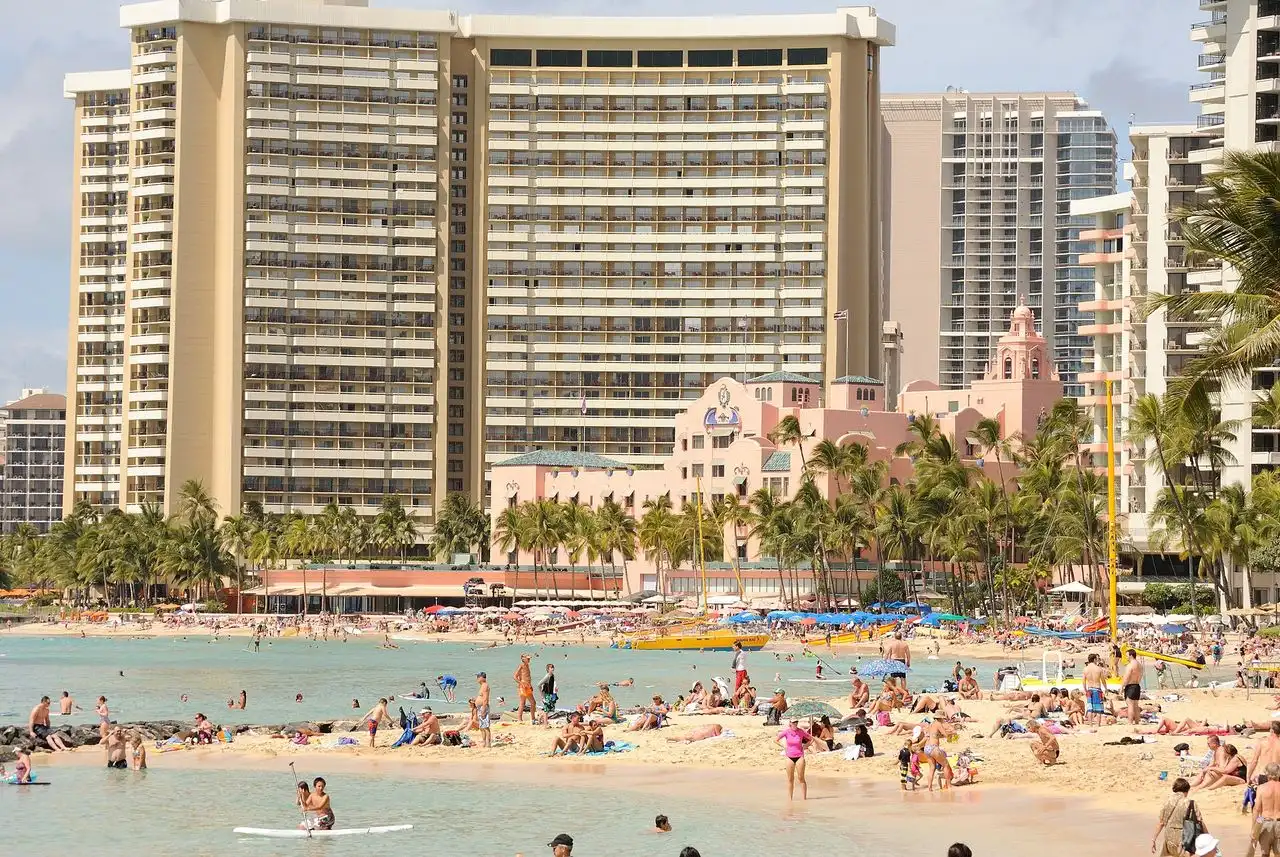 Sunbathers and swimmers packed onto Waikiki Beach in Honolulu with hotel towers behind