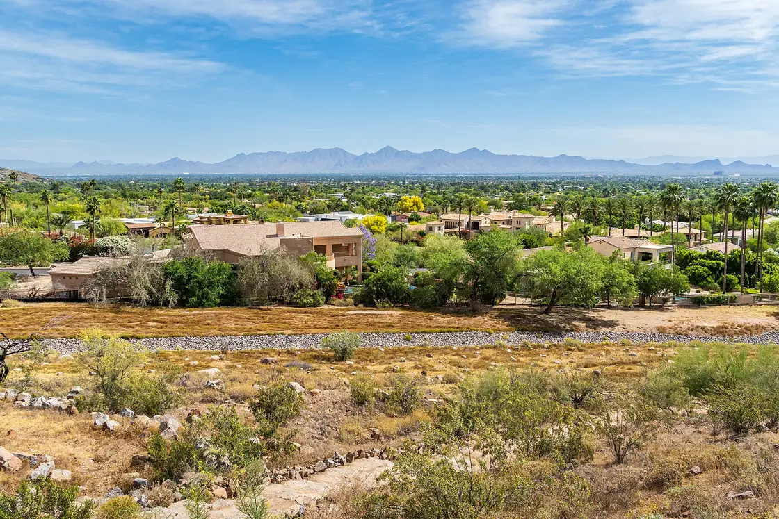 Tan houses and palm trees on a dry slope, with the Phoenix valley and distant mountains beyond