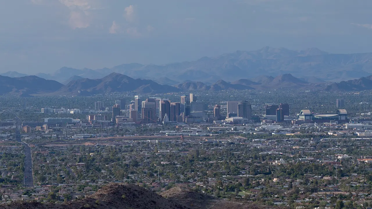 Phoenix from a desert hillside in daylight: valley sprawl, downtown towers and Chase Field, mountains in haze