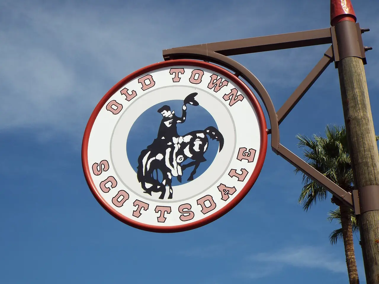 Circular Old Town Scottsdale sign with a bucking-bronco silhouette on a pole against blue sky