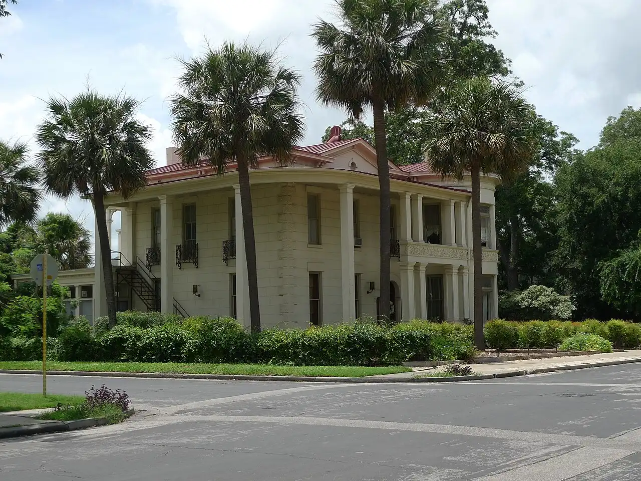 Cream historic mansion with wraparound porch columns and palm trees in San Antonio King William District