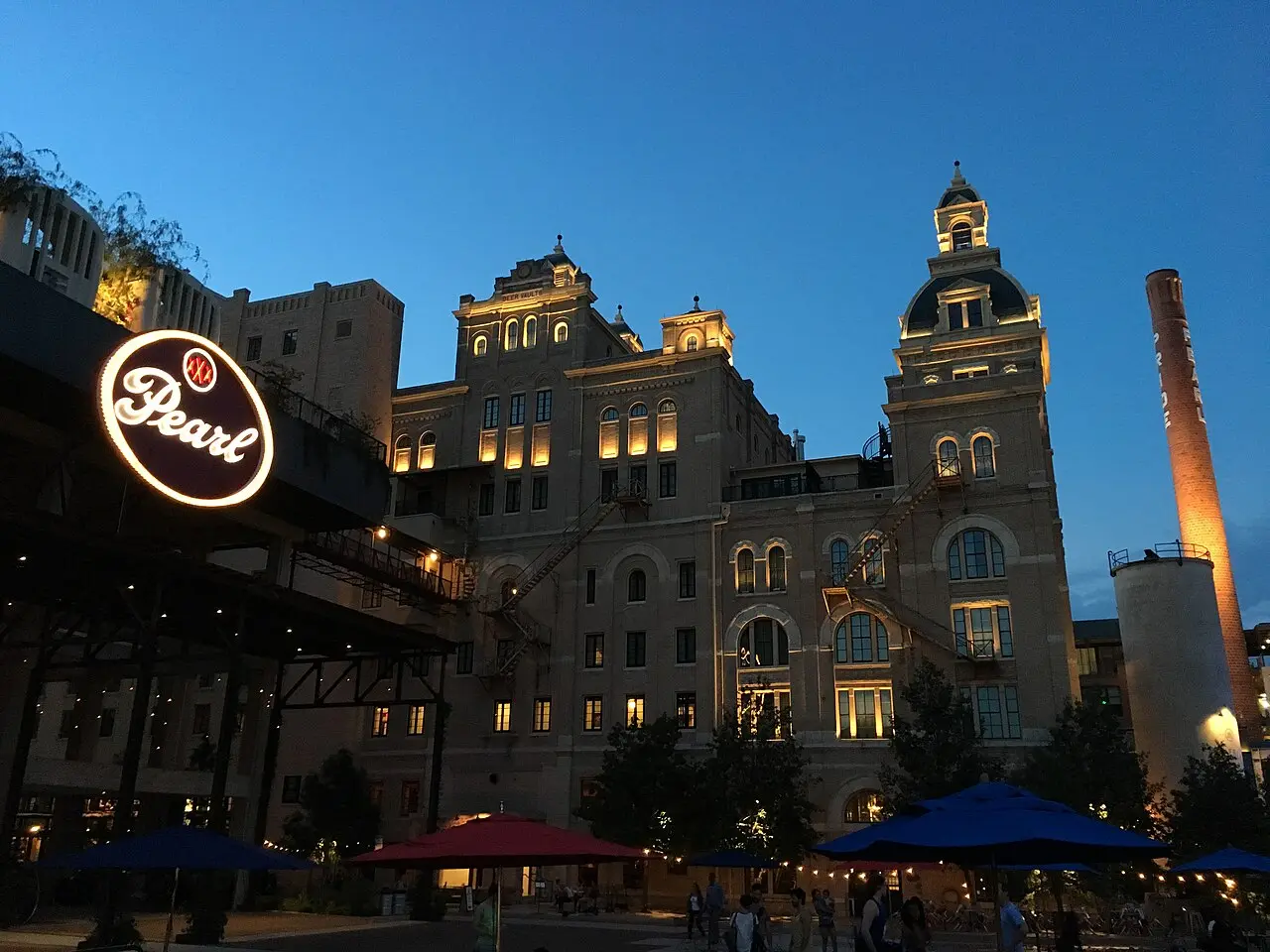Illuminated Pearl Brewery building, neon Pearl sign and plaza umbrellas at twilight in San Antonio