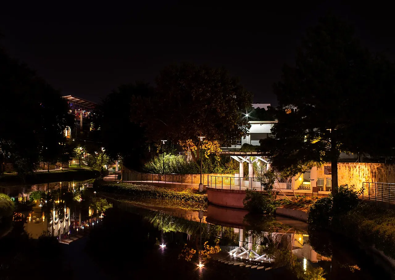 Restaurant lights and cypress trees reflected in the San Antonio River Walk at dusk