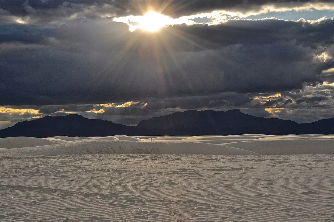 Sunlight breaking through clouds over white sand dunes