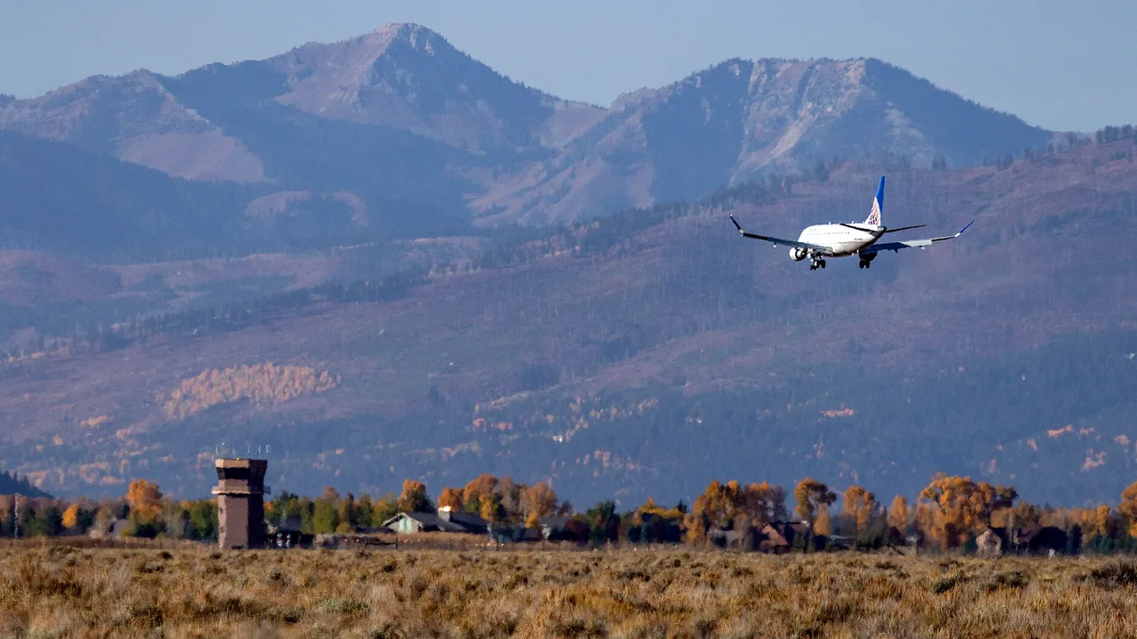 An aircraft landing at Jackson Hole Airport with the Teton Range rising behind the runway